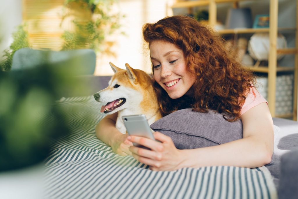 Woman sitting outdoors with her Shiba Inu while browsing her phone